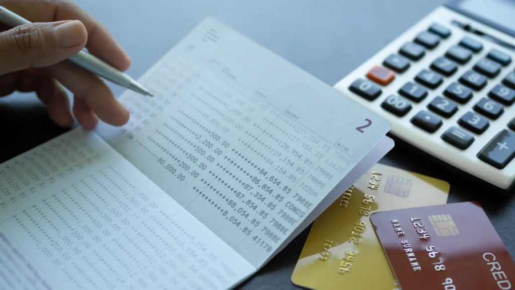 Finger holding pen poin number on book bank with caculator credit card.